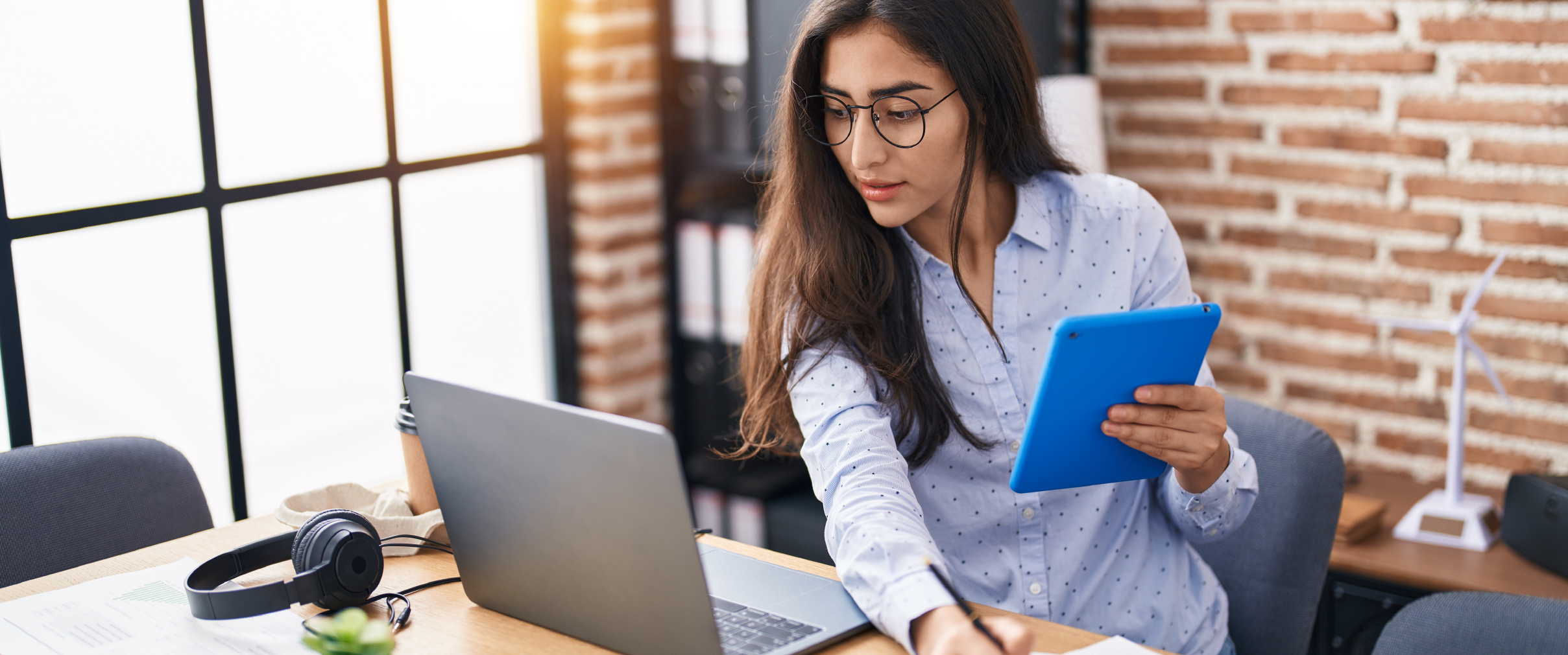 A woman using her tablet and laptop to work. 
