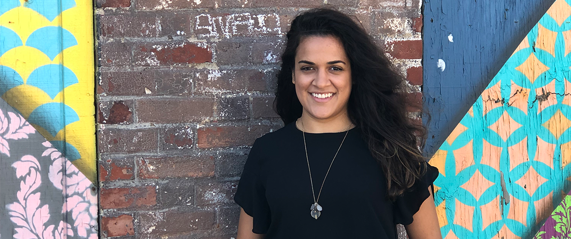 Carly de la Hoz: Headshot of woman standing in front of colorful brick wall