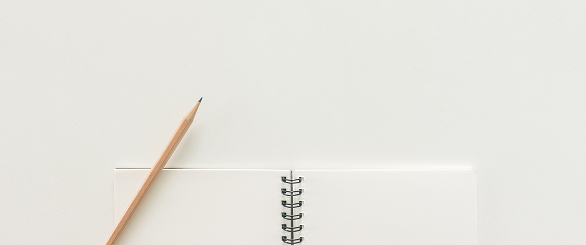 A number 2 pencil sits on top of a blank notebook on a white desk.