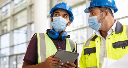 Two architects on a construction site wearing face coverings.