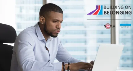 An architect in a firm office is sitting at a desk while typing on a laptop.