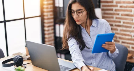 A woman using her tablet and laptop to work. 