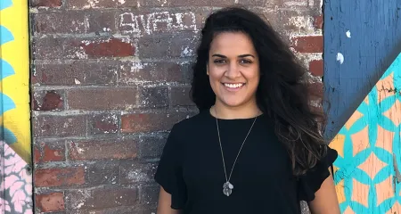 Carly de la Hoz: Headshot of woman standing in front of colorful brick wall