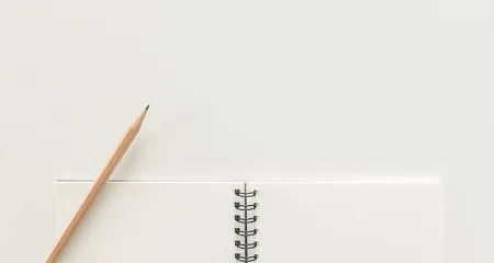A number 2 pencil sits on top of a blank notebook on a white desk.