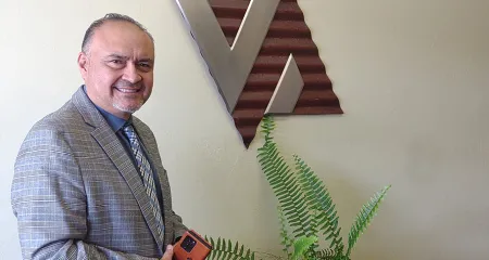 Architect Ray Vigil stands in front of his firm's logo.