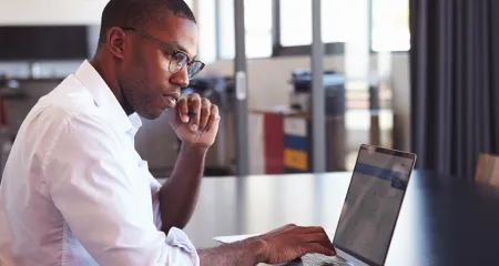 A man of color looking at his laptop. 