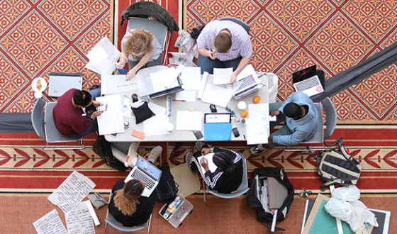 A group of students sketch and work on laptops at a table during a design competition sponsored by NCARB.