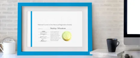 A framed NCARB Certificate sits on a desk.