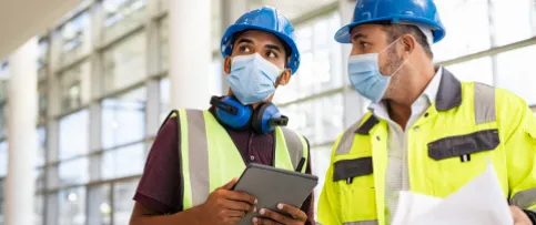 Two architects on a construction site wearing face coverings.