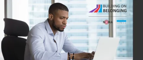 An architect in a firm office is sitting at a desk while typing on a laptop.