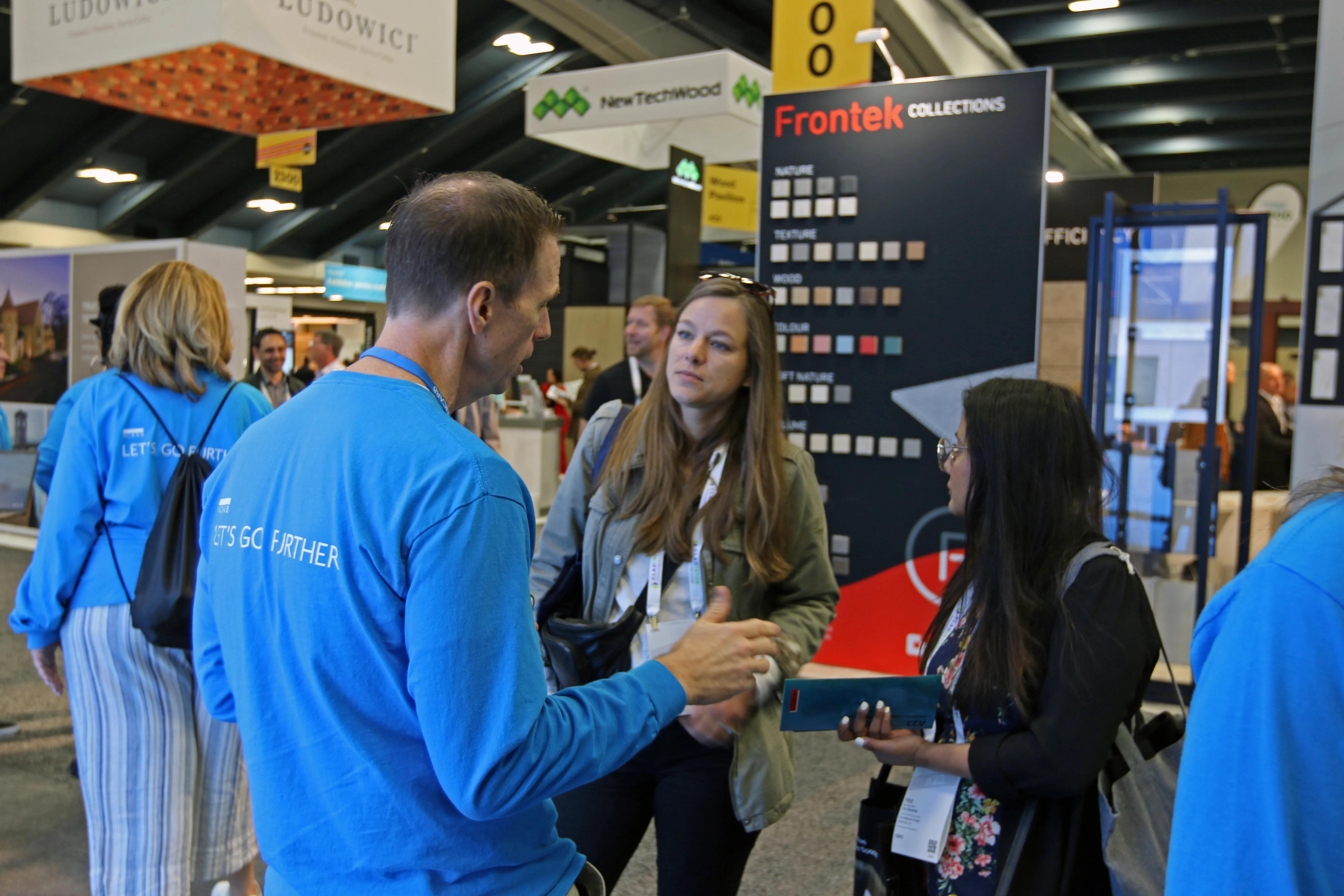 An NCARB staff member in a blue NCARB shirt talks to two women at NCARB's A'23 booth.