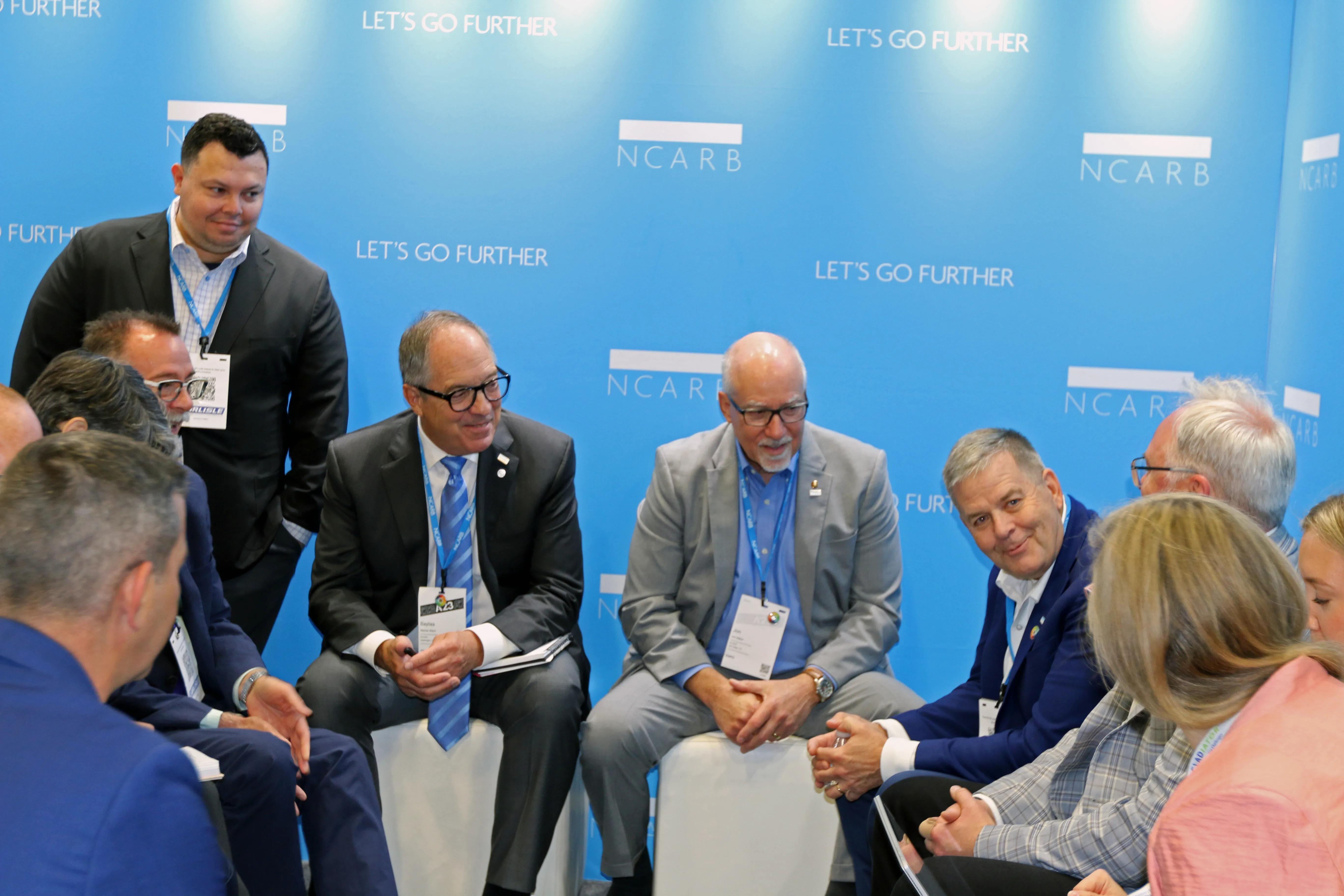NCARB leaders and other regulatory body leaders are talking together while sitting on white stools.
