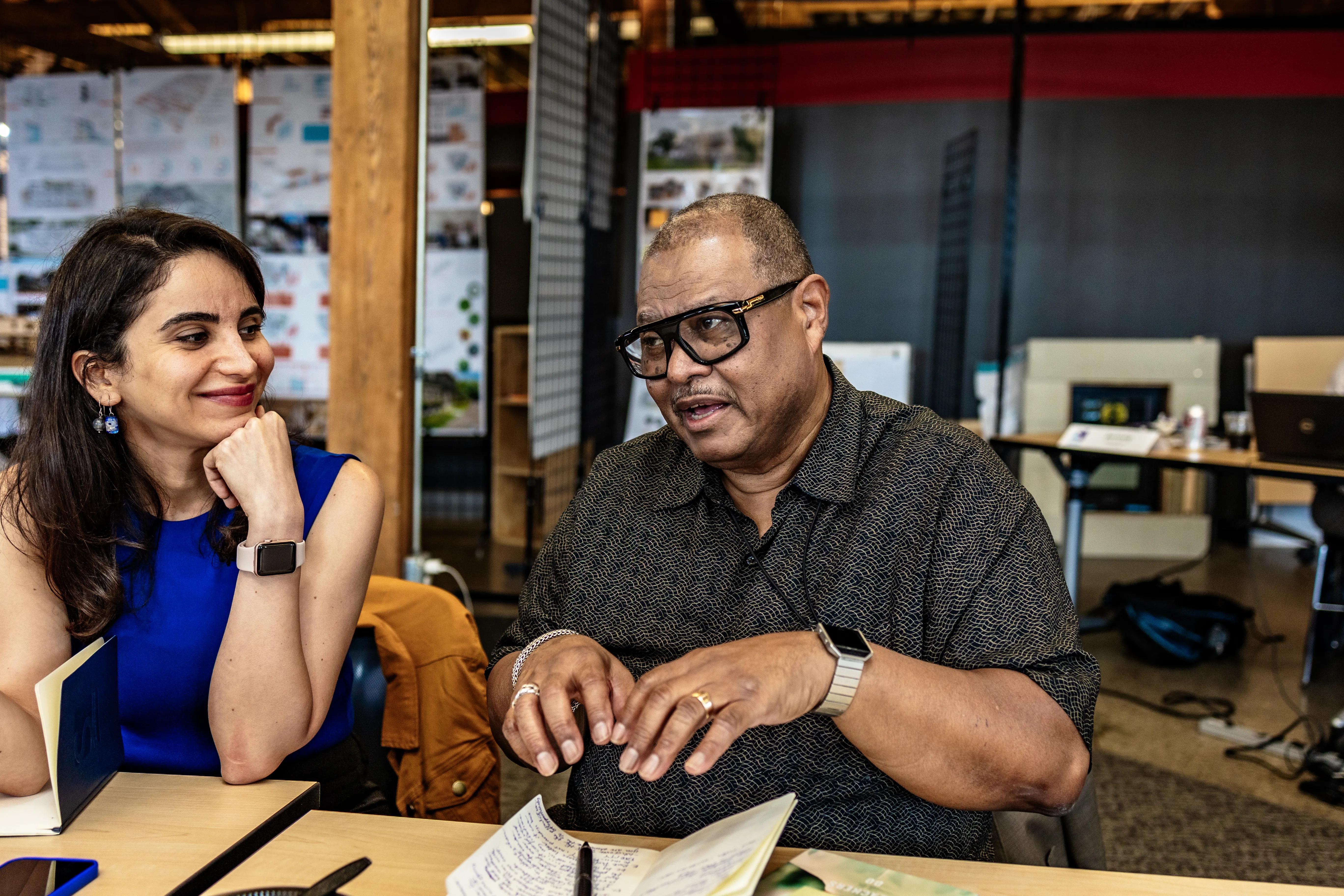 A woman and a man are talking while sitting at a table with their notebooks open.