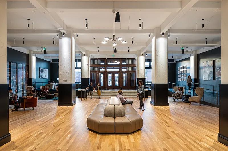 An apartment lobby with big windows and various seating areas where people are gathered and talking.